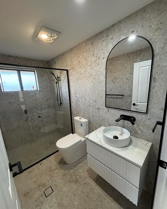 Renovated bathroom with a frameless glass shower, arched mirror and white floating vanity